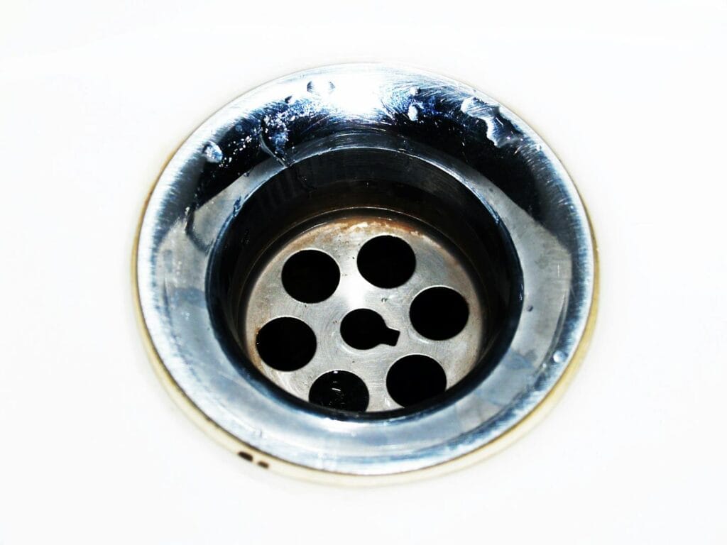 Detailed image of a chrome sink drain showcasing water droplets and a metallic finish.
