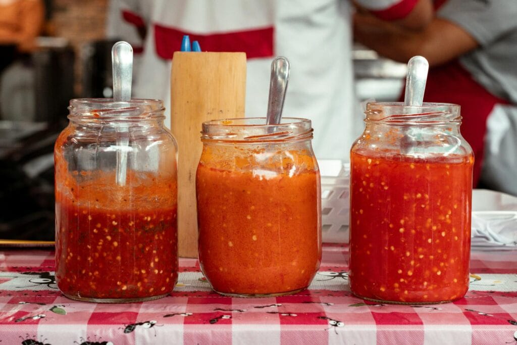 A close-up of three jars filled with vibrant red chili sauces on a red and white checkered tablecloth.