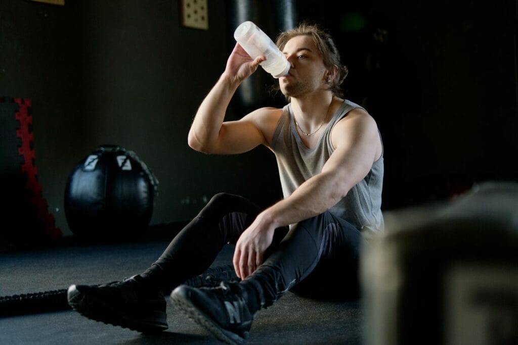 An athletic man in a gym taking a break and drinking water post workout for hydration.