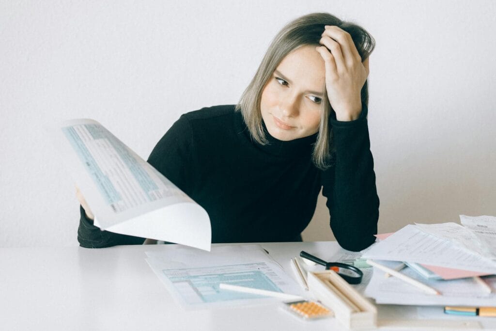 A woman showing stress while reviewing multiple paperwork and financial documents at a desk.