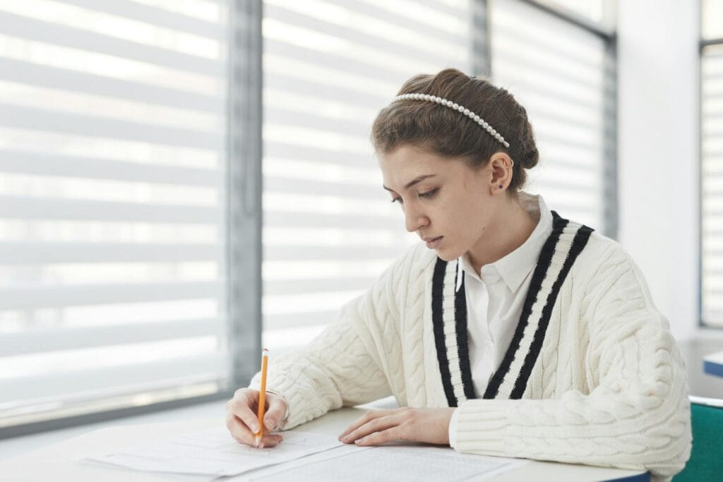 A student intensely focused on writing during an exam in a bright classroom setting.
