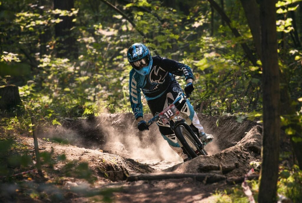 A biker navigates a challenging dirt trail in a vibrant forest, showcasing speed and skill.