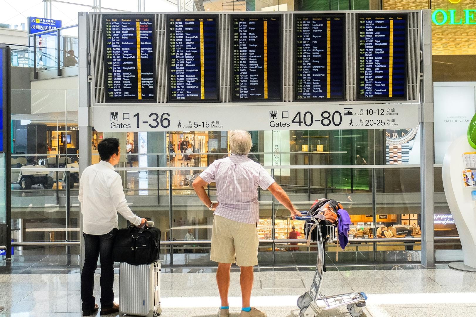 Passengers review flight information on a digital board in Hong Kong airport terminal.